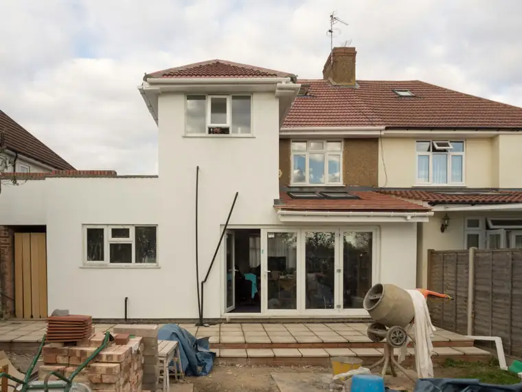 Extension en cours à l’arrière d’une maison : nouvelles baies, bétonnière et matériaux au sol